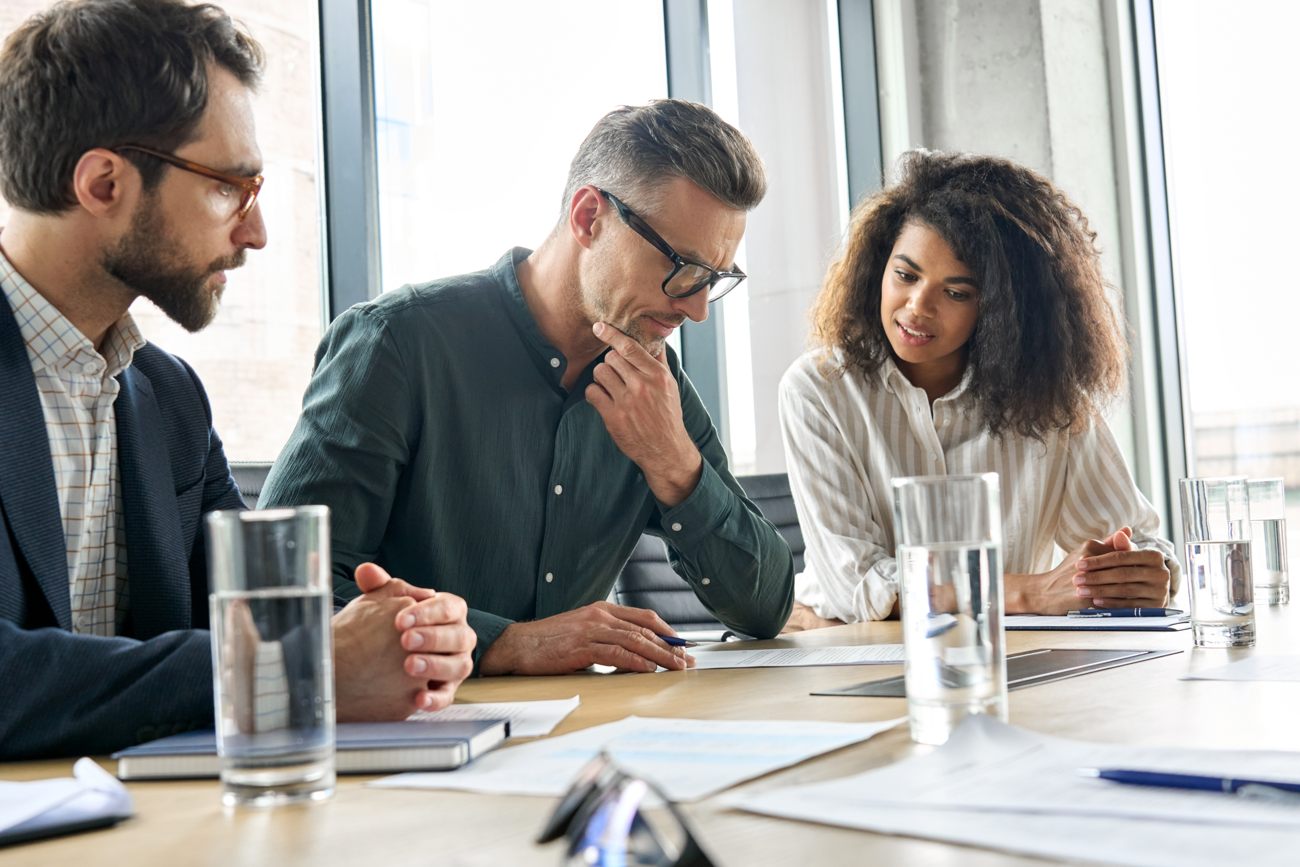 Three people sitting at an office table discussing paperwork