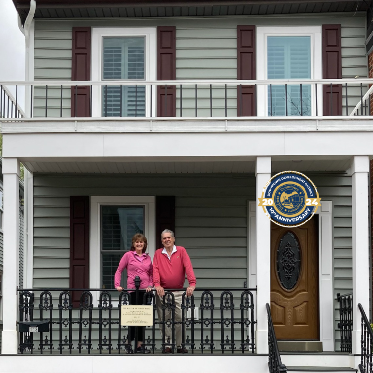 The couple standing on the porch of their historic home after using the Downtown Development Districts program.