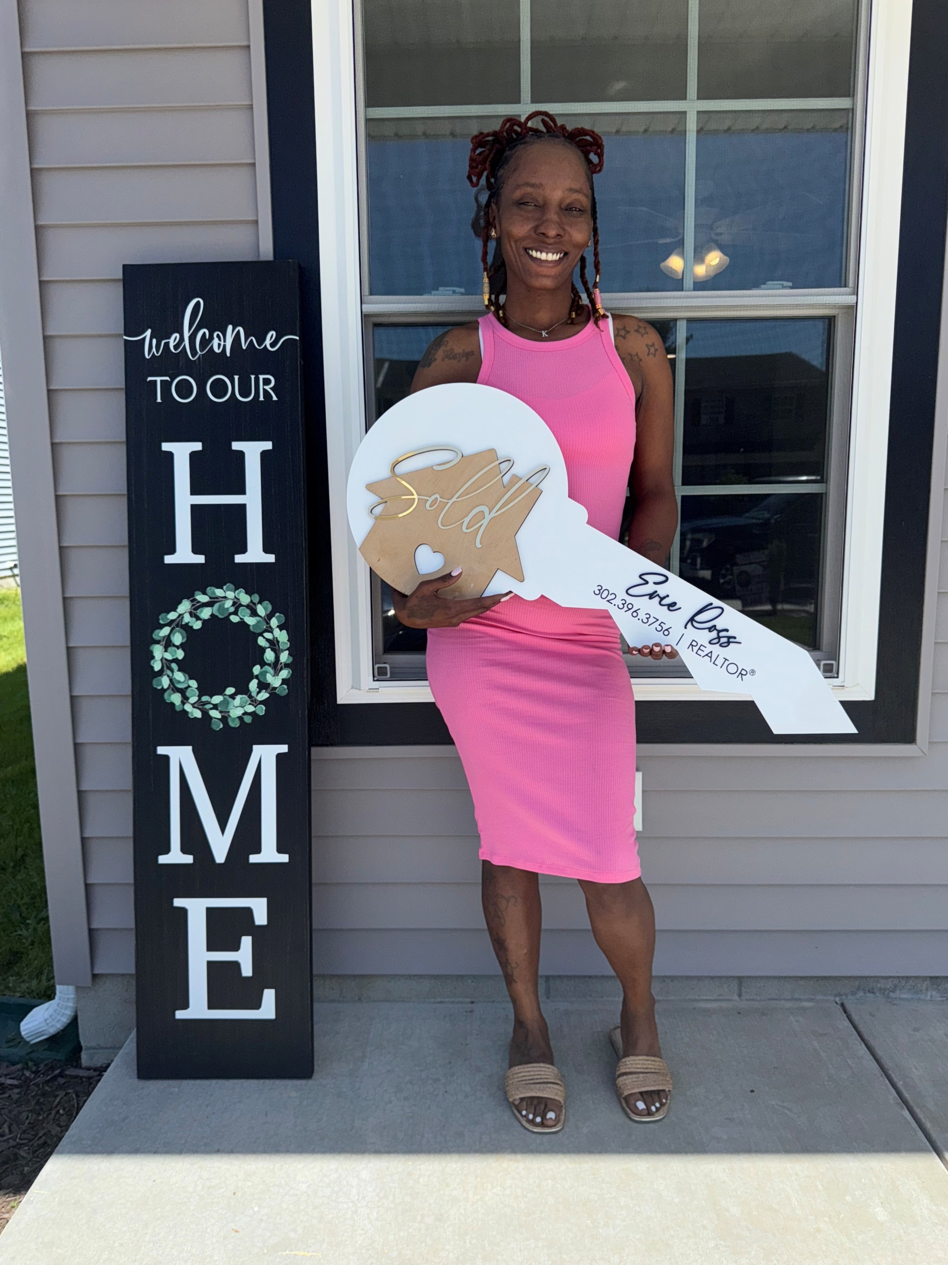 Krystal Dean standing in front of her new home with a large key sign.