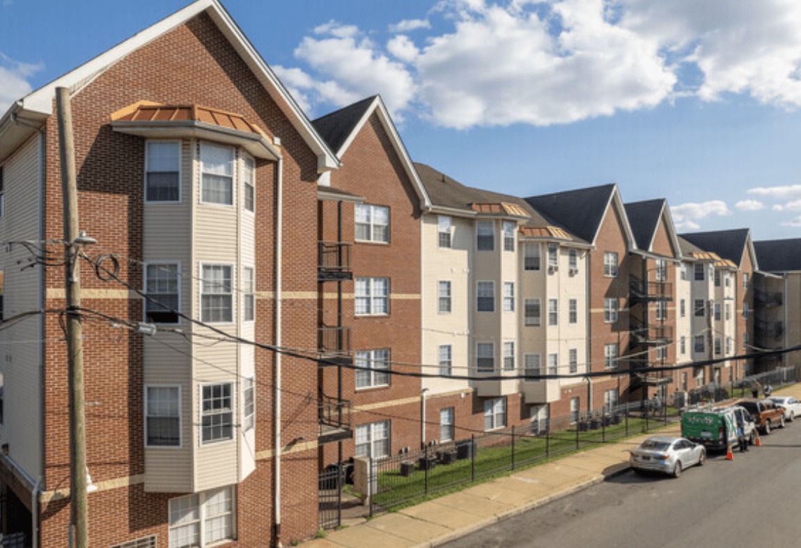 Row of brick and tan-siding apartment buildings along a residential street on a sunny day