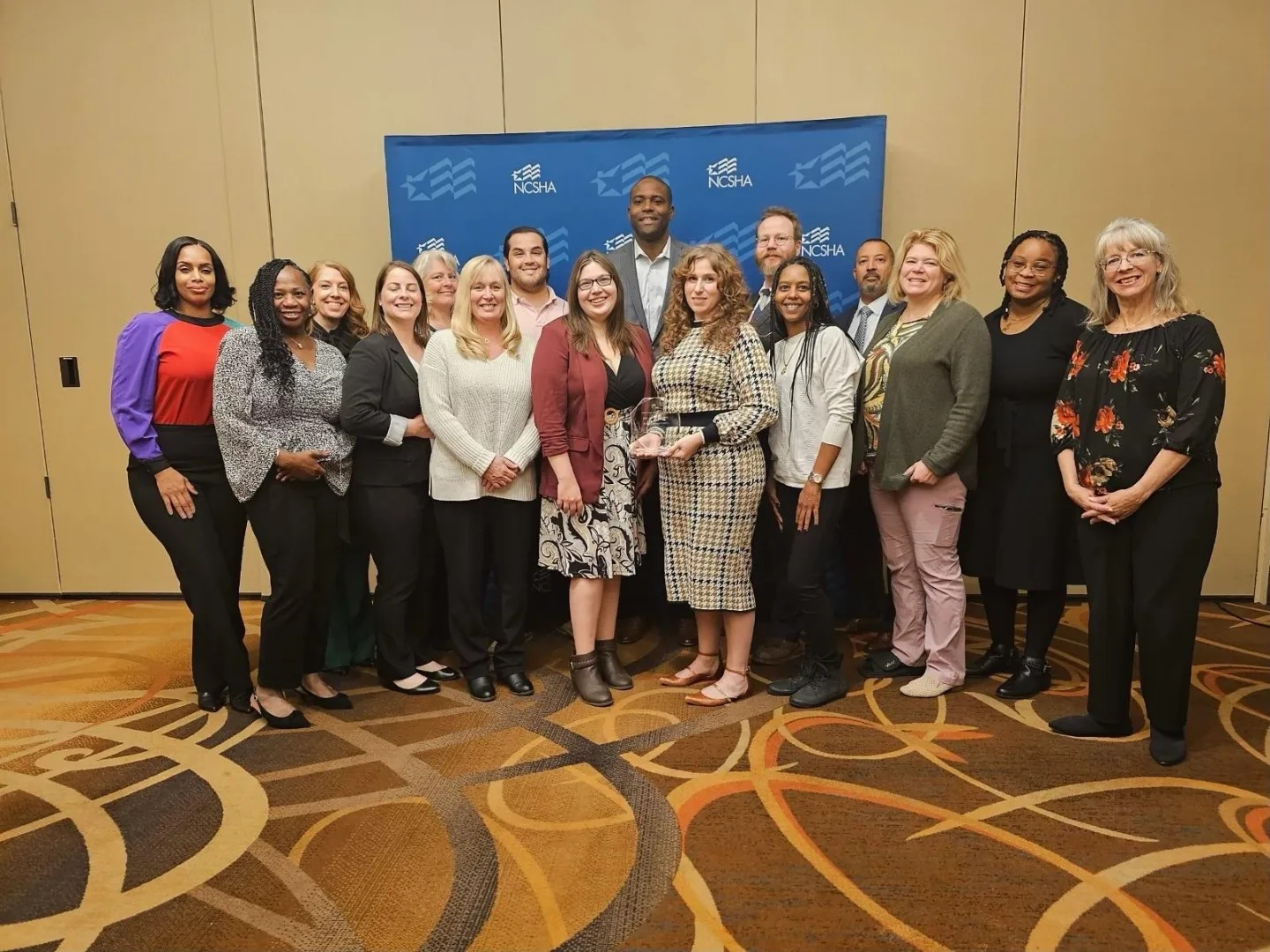 DSHA staff gathered in front of an NCSHA backdrop to celebrate the agency’s national award
