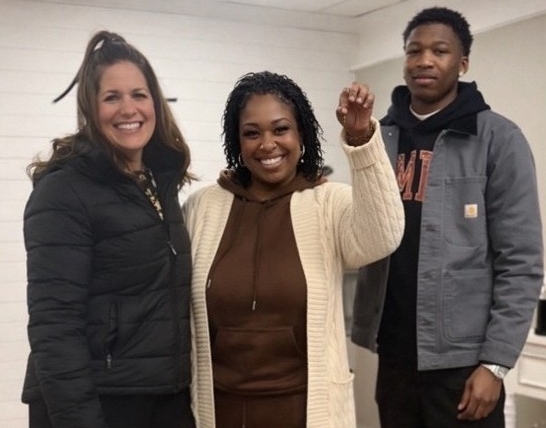 Debra Mack holding up the keys to her new home alongside two supporters