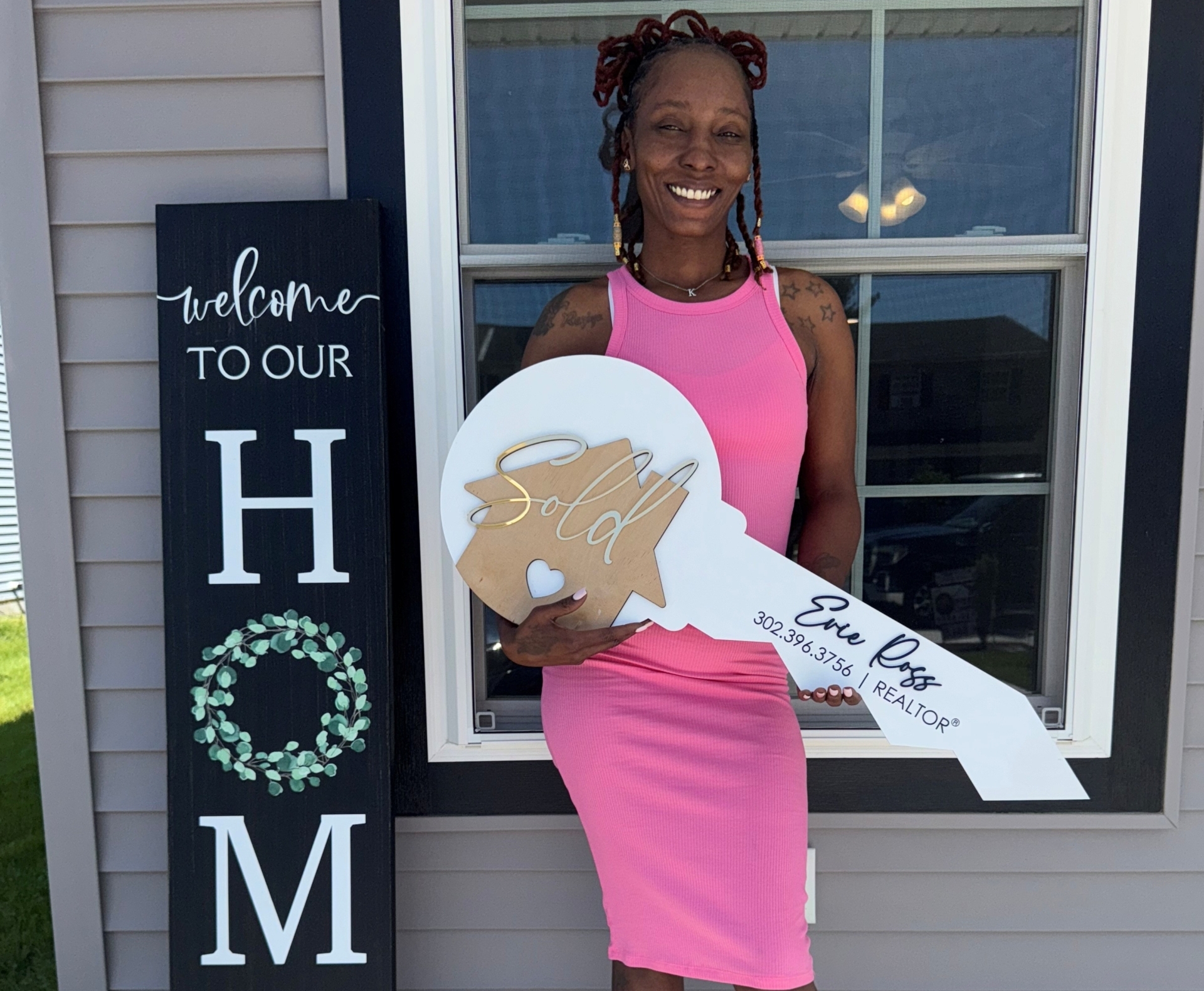 Krystal Dean holding a large sold key sign outside the window of her new home
