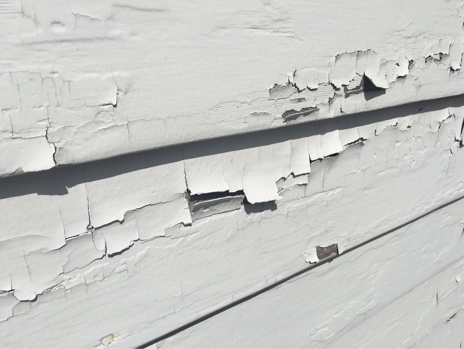 White paint peeling and flaking from the wooden clapboard siding of an older home