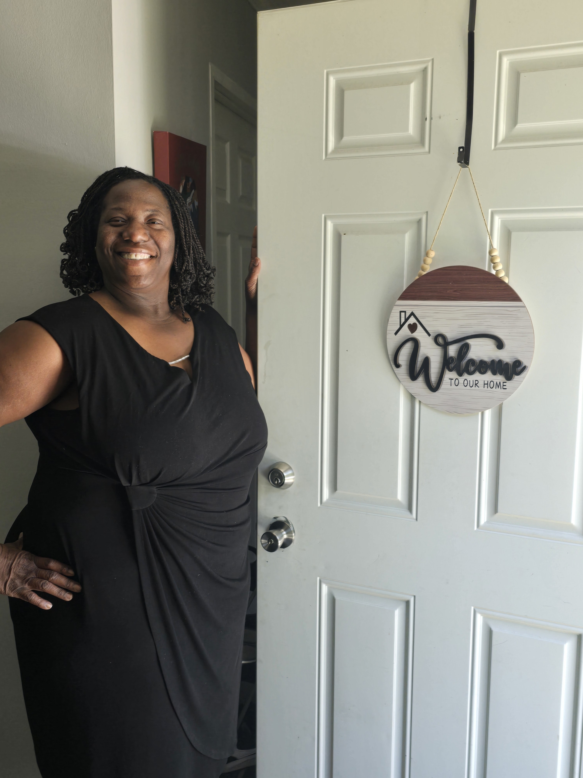 Petric Handy smiling at the front door of her new home beside a welcome sign