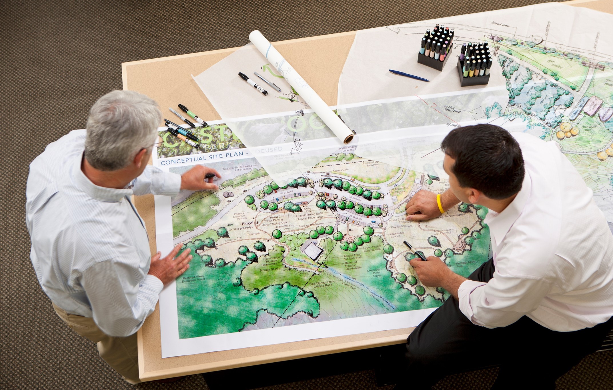 Two planners reviewing and marking up a conceptual site plan spread across a work table
