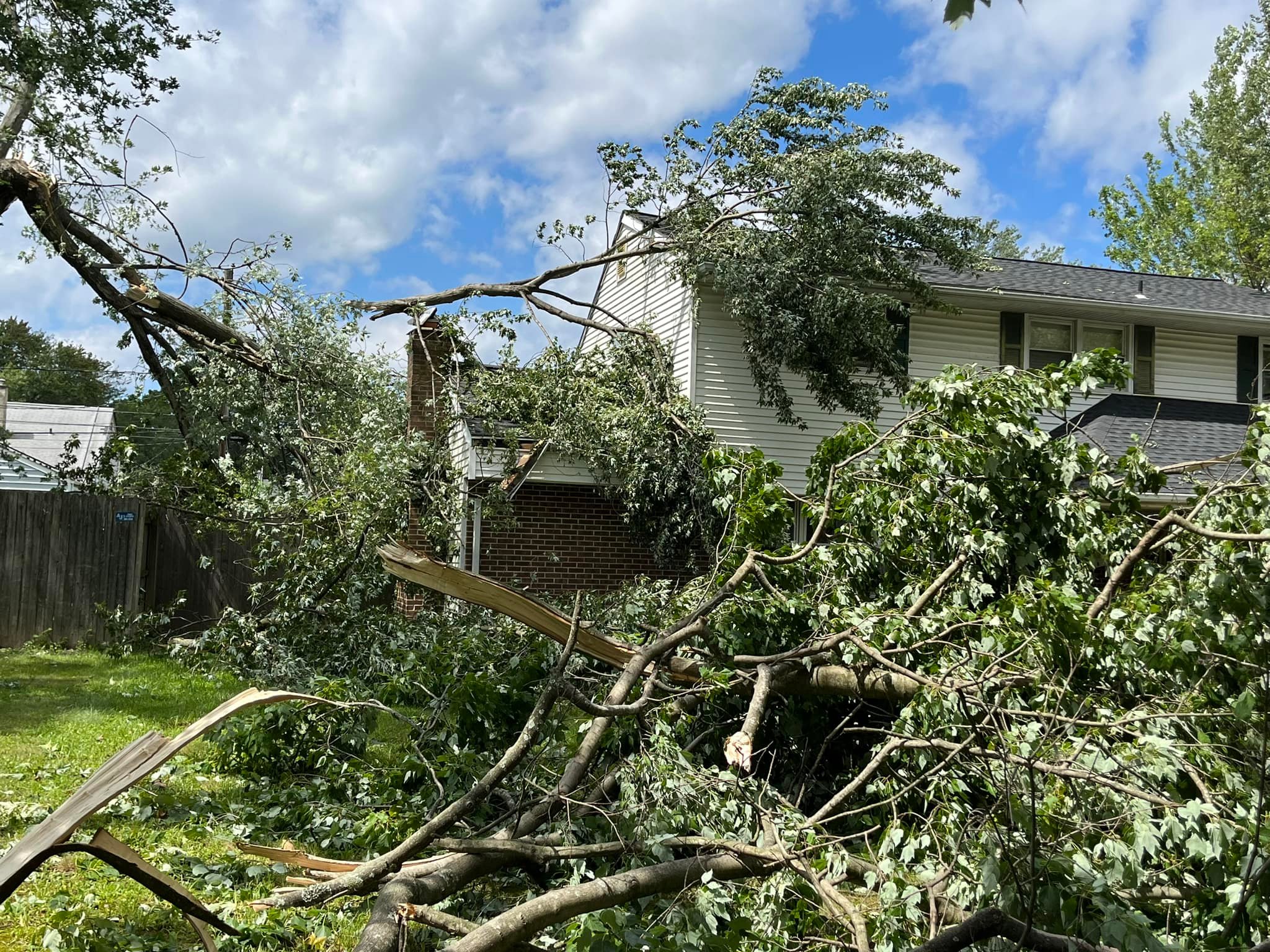 Fallen tree limbs covering the yard of a two-story house after a storm